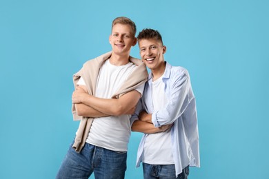 Happy brothers posing with crossed arms on light blue background