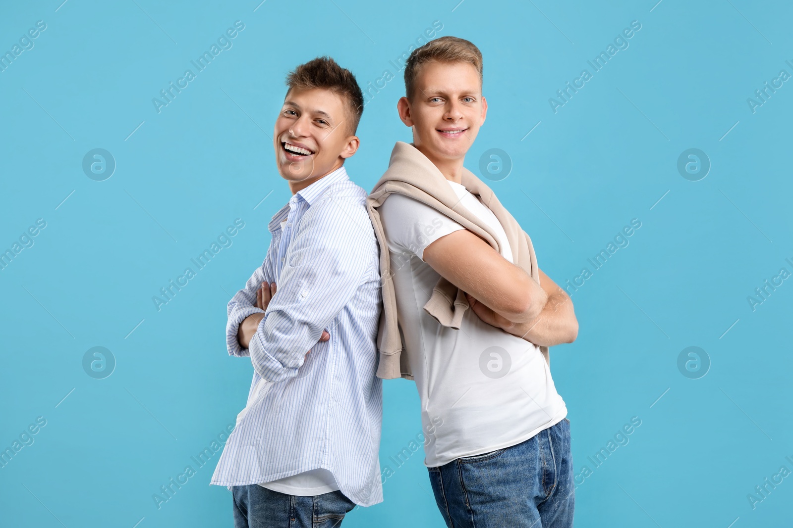 Photo of Happy brothers posing with crossed arms on light blue background