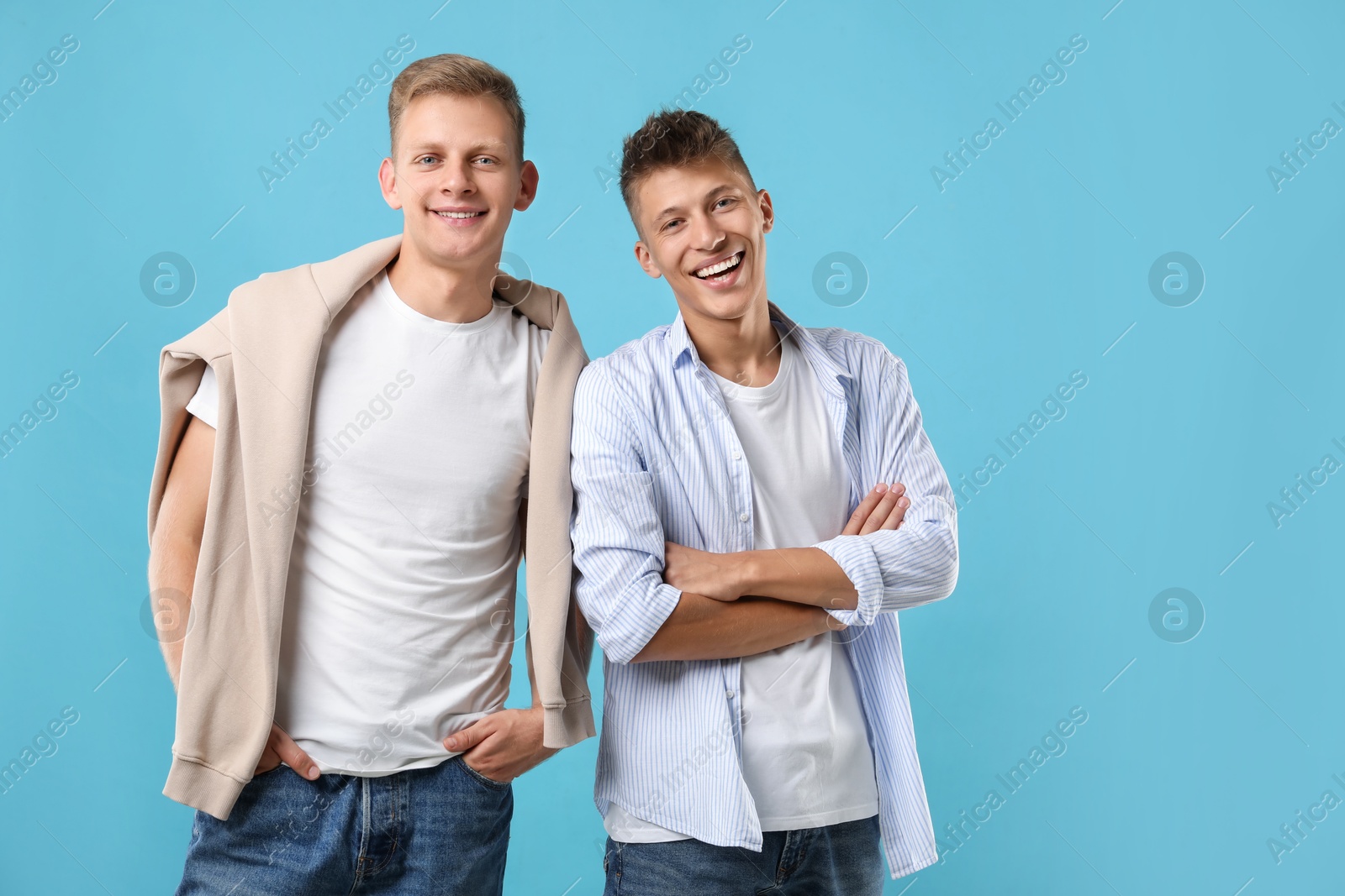 Photo of Young brothers posing with crossed arms on light blue background. Space for text