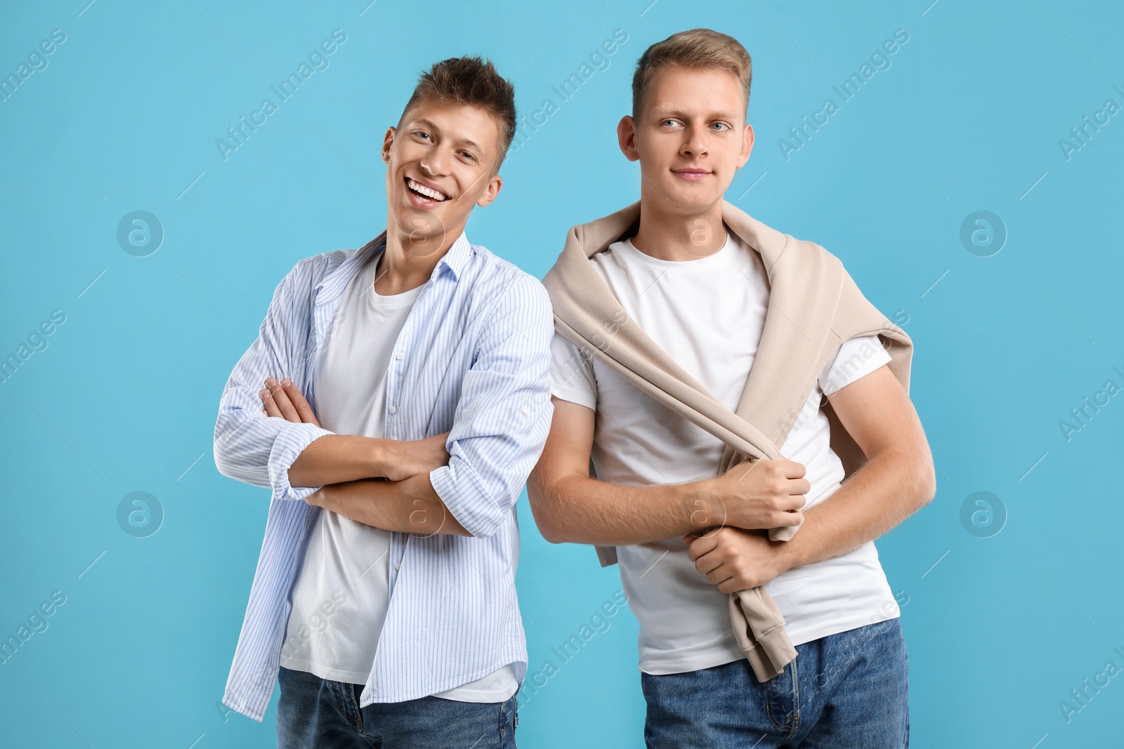 Photo of Young brothers posing with crossed arms on light blue background. Space for text