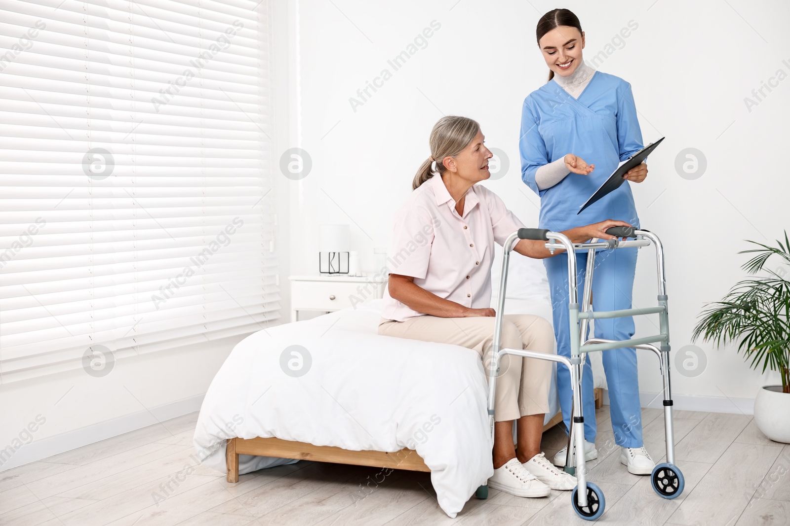 Photo of Nurse helping senior woman with walking frame in clinic