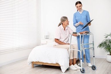 Photo of Nurse helping senior woman with walking frame in clinic