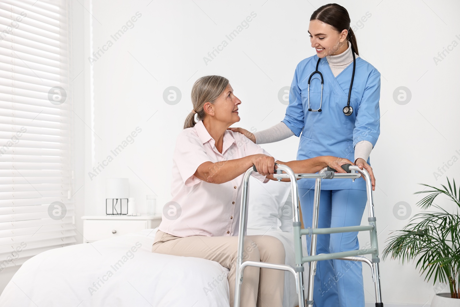 Photo of Nurse helping senior woman with walking frame in clinic