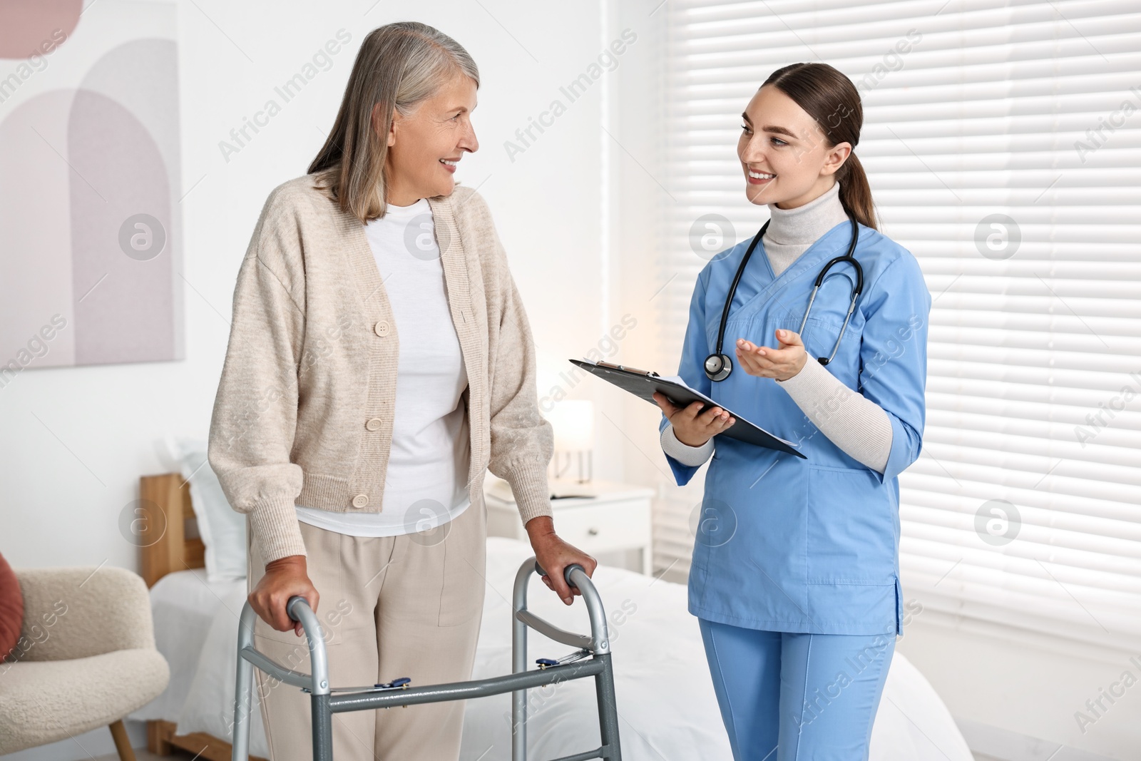 Photo of Nurse helping senior woman with walking frame in clinic