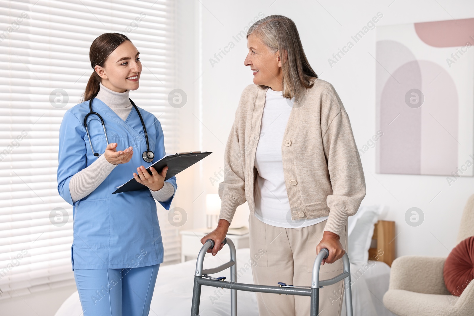 Photo of Nurse helping senior woman with walking frame in clinic