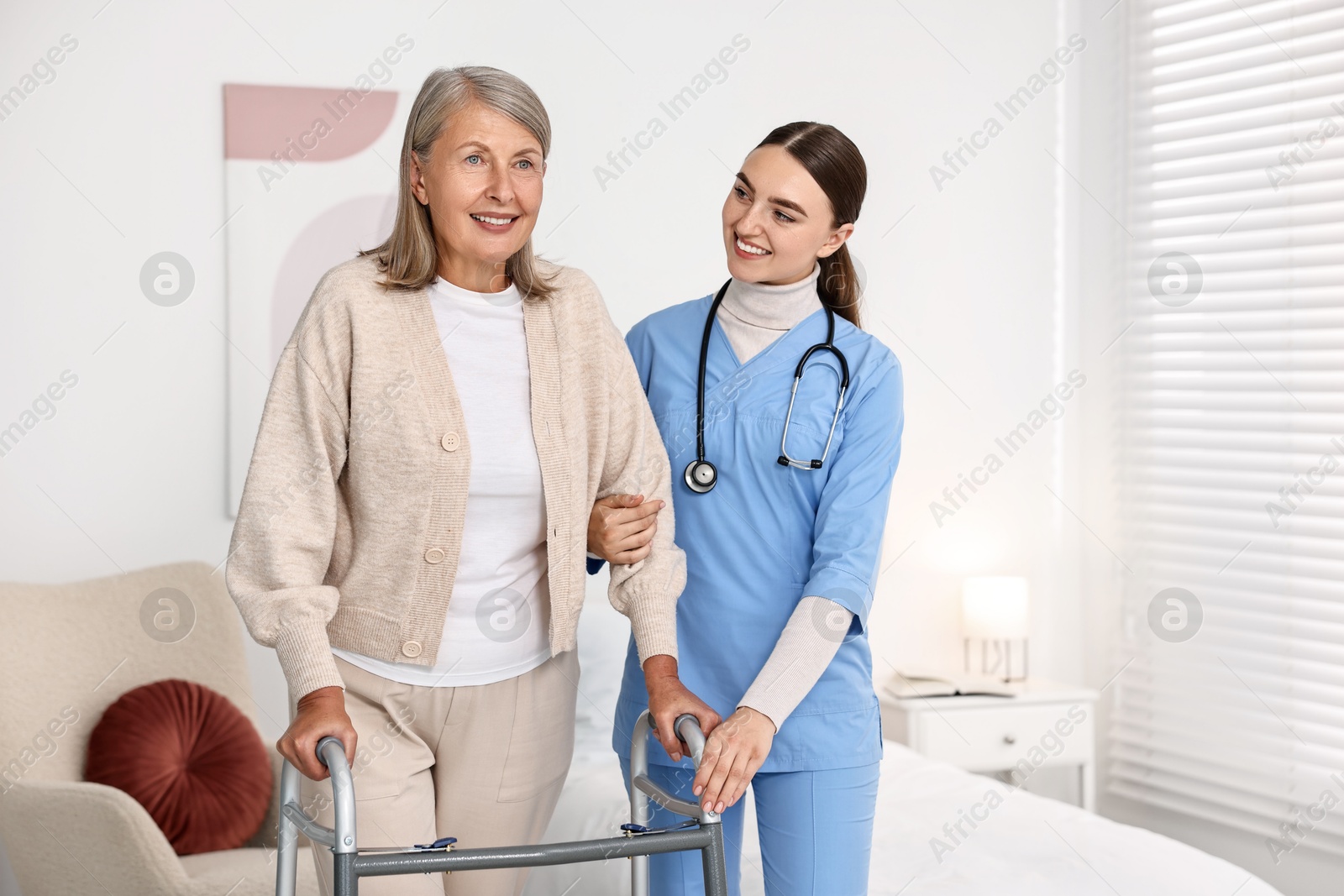 Photo of Nurse helping senior woman with walking frame in clinic