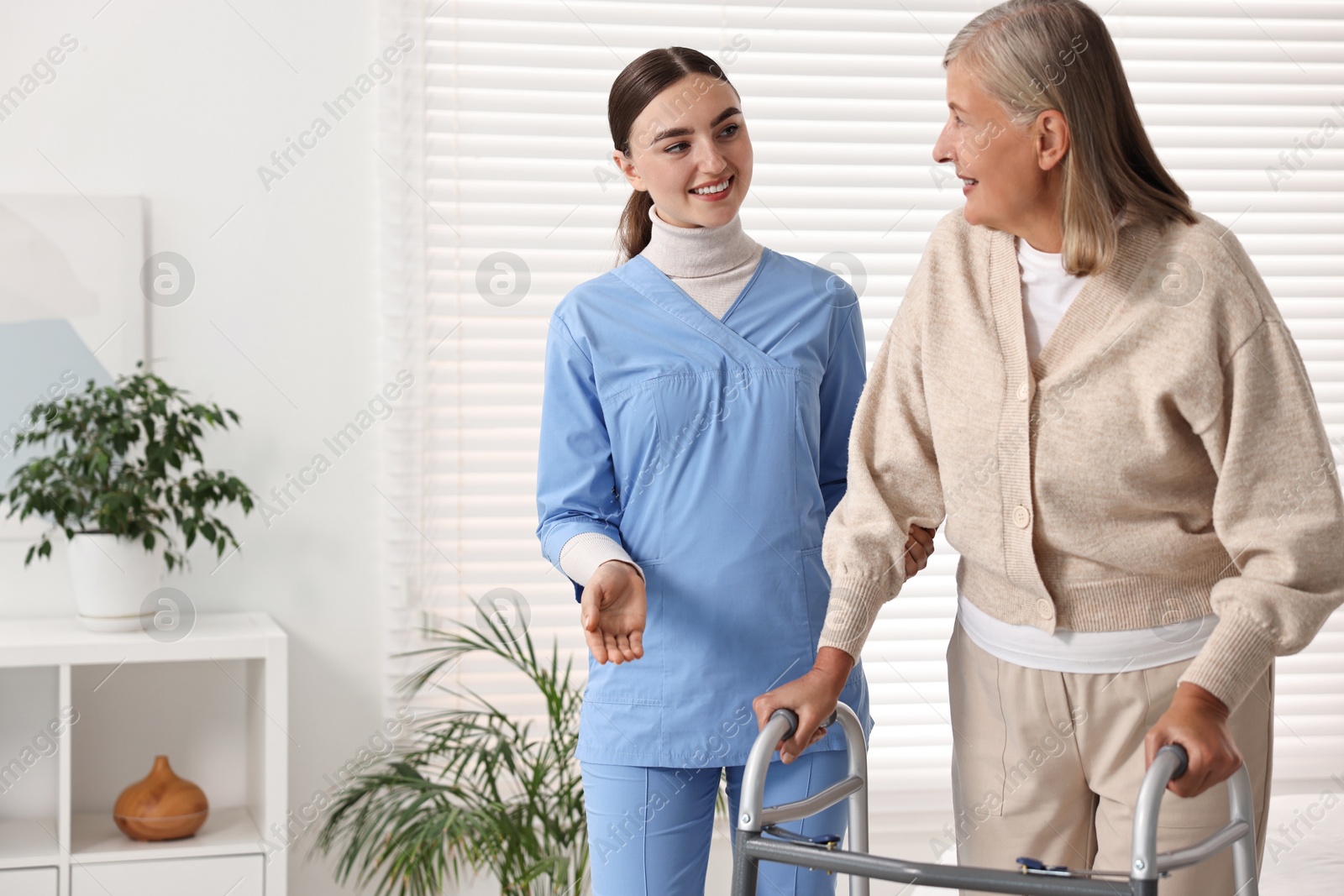 Photo of Nurse helping senior woman with walking frame in clinic