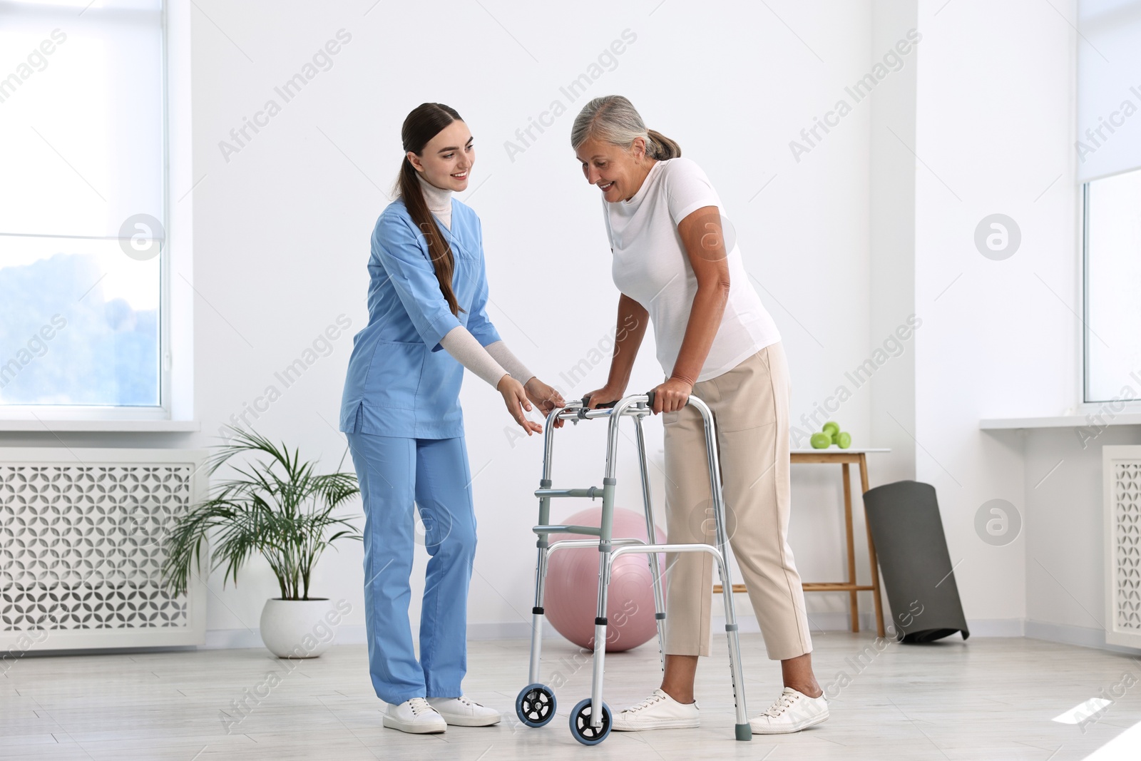 Photo of Nurse helping senior woman with walking frame in clinic