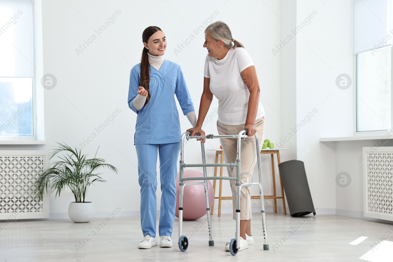 Photo of Nurse helping senior woman with walking frame in clinic