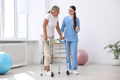 Nurse helping senior woman with walking frame in clinic