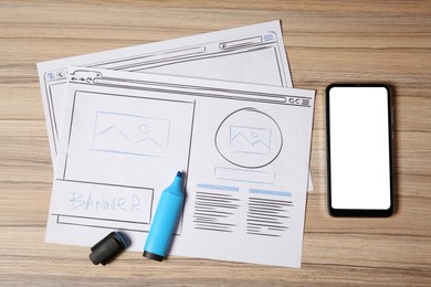 Photo of Website development. Sketches of wireframes, highlighter and smartphone on wooden table, flat lay