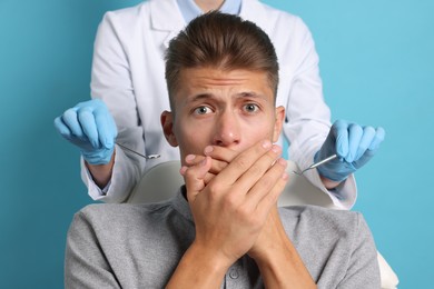 Photo of Dental phobia. Dentist working with scared man on light blue background, closeup