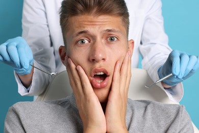 Dental phobia. Dentist working with scared man on light blue background, closeup