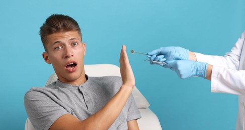 Photo of Dental phobia. Dentist working with scared man on light blue background, closeup