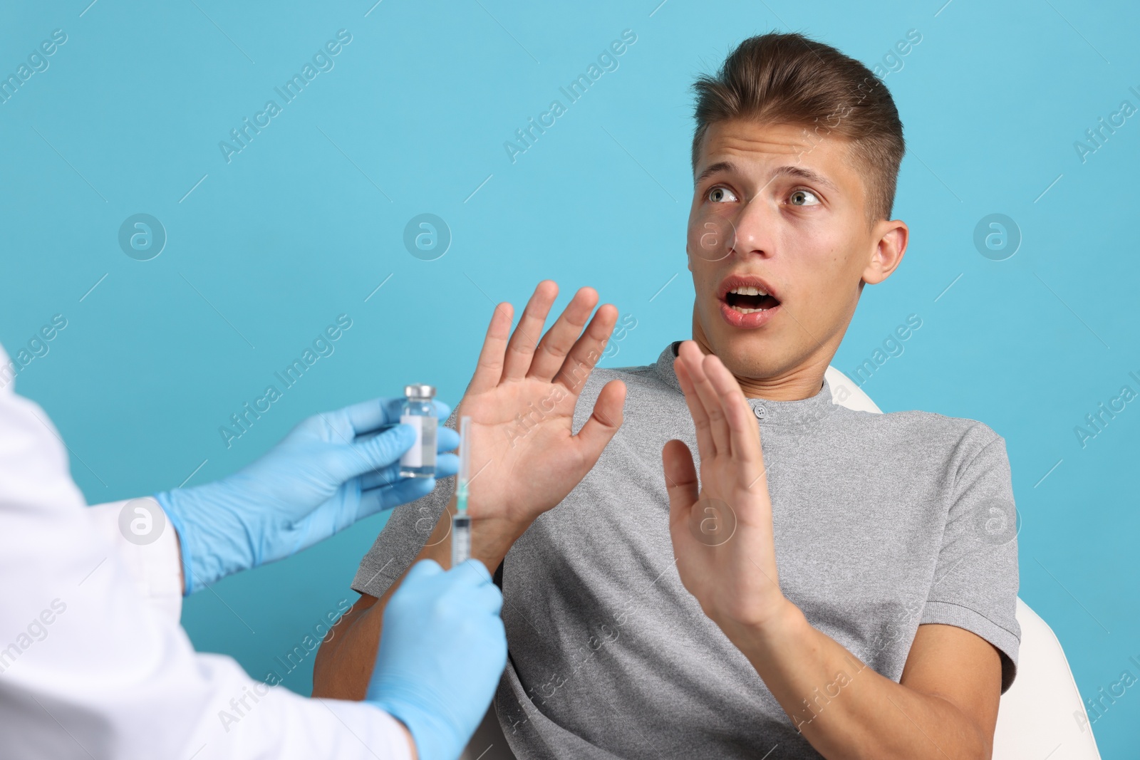 Photo of Needle phobia. Scared man making stop gesture near doctor with syringe and vial on light blue background