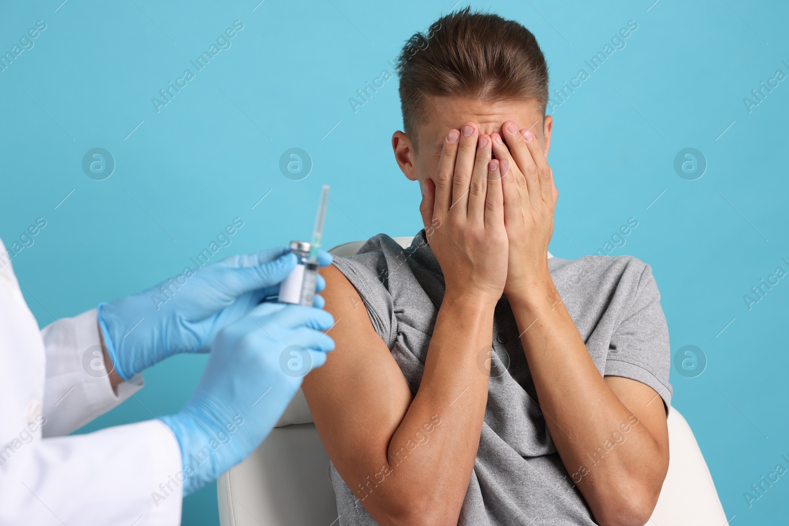 Photo of Needle phobia. Doctor with syringe and vial near scared man on light blue background, closeup