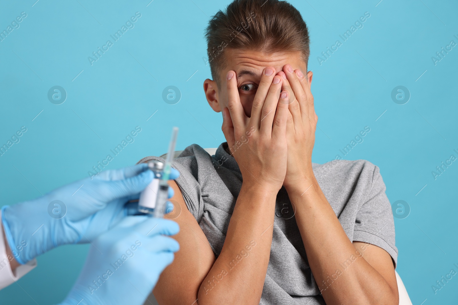 Photo of Needle phobia. Doctor with syringe and vial near scared man on light blue background, closeup