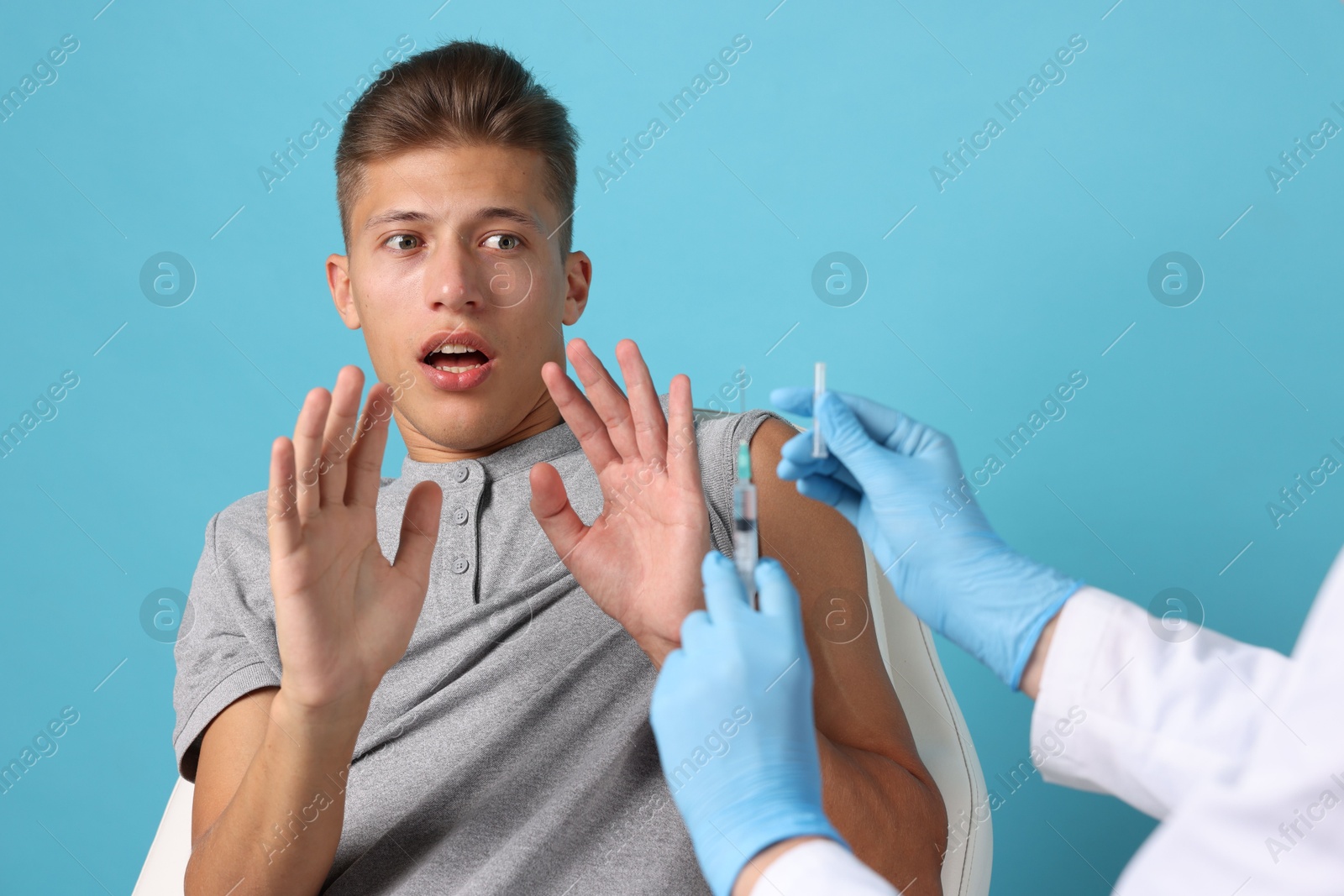 Photo of Needle phobia. Scared man making stop gesture near doctor with syringe and vial on light blue background