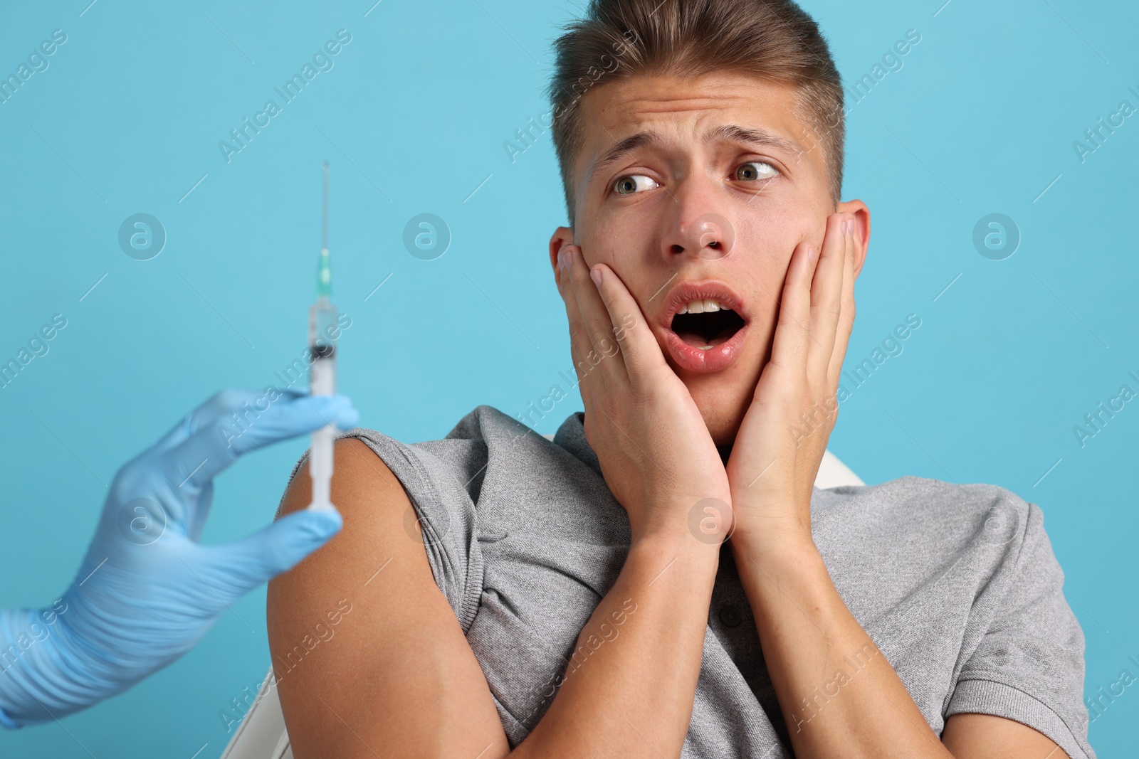 Photo of Needle phobia. Doctor with syringe near scared man on light blue background, closeup