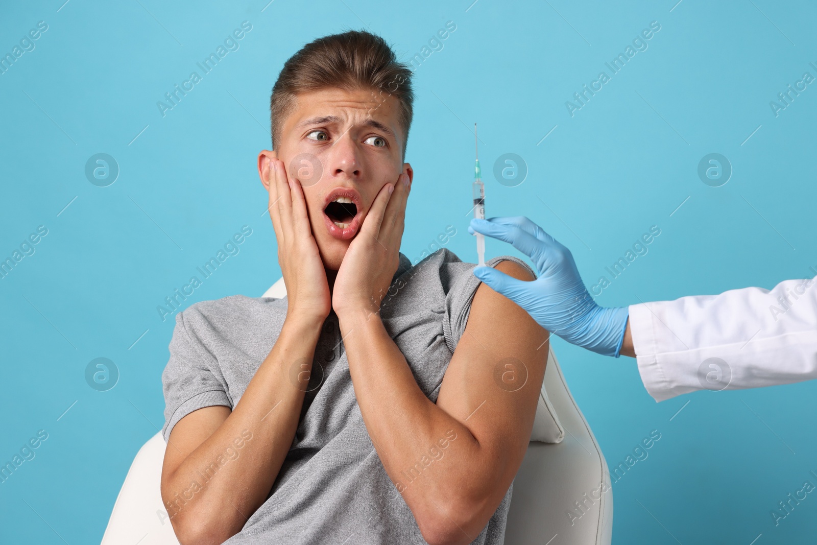 Photo of Needle phobia. Doctor with syringe near scared man on light blue background, closeup