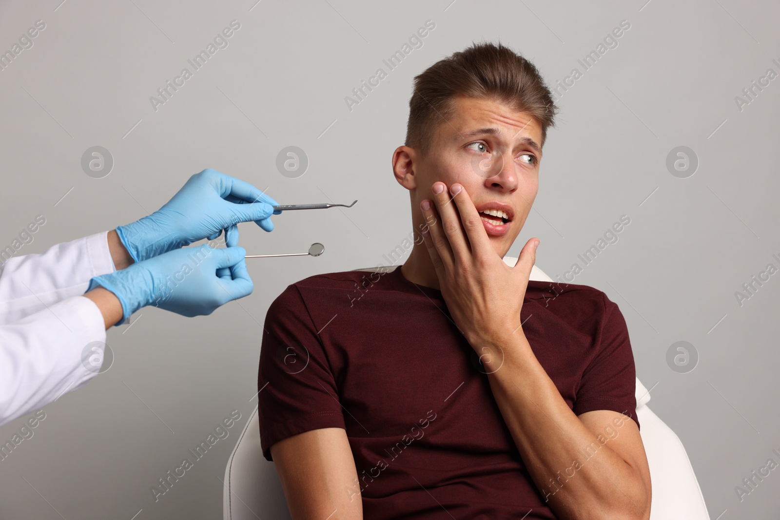 Photo of Dental phobia. Dentist working with scared man on grey background, closeup