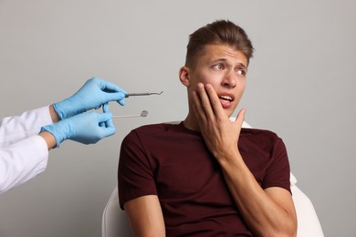 Photo of Dental phobia. Dentist working with scared man on grey background, closeup