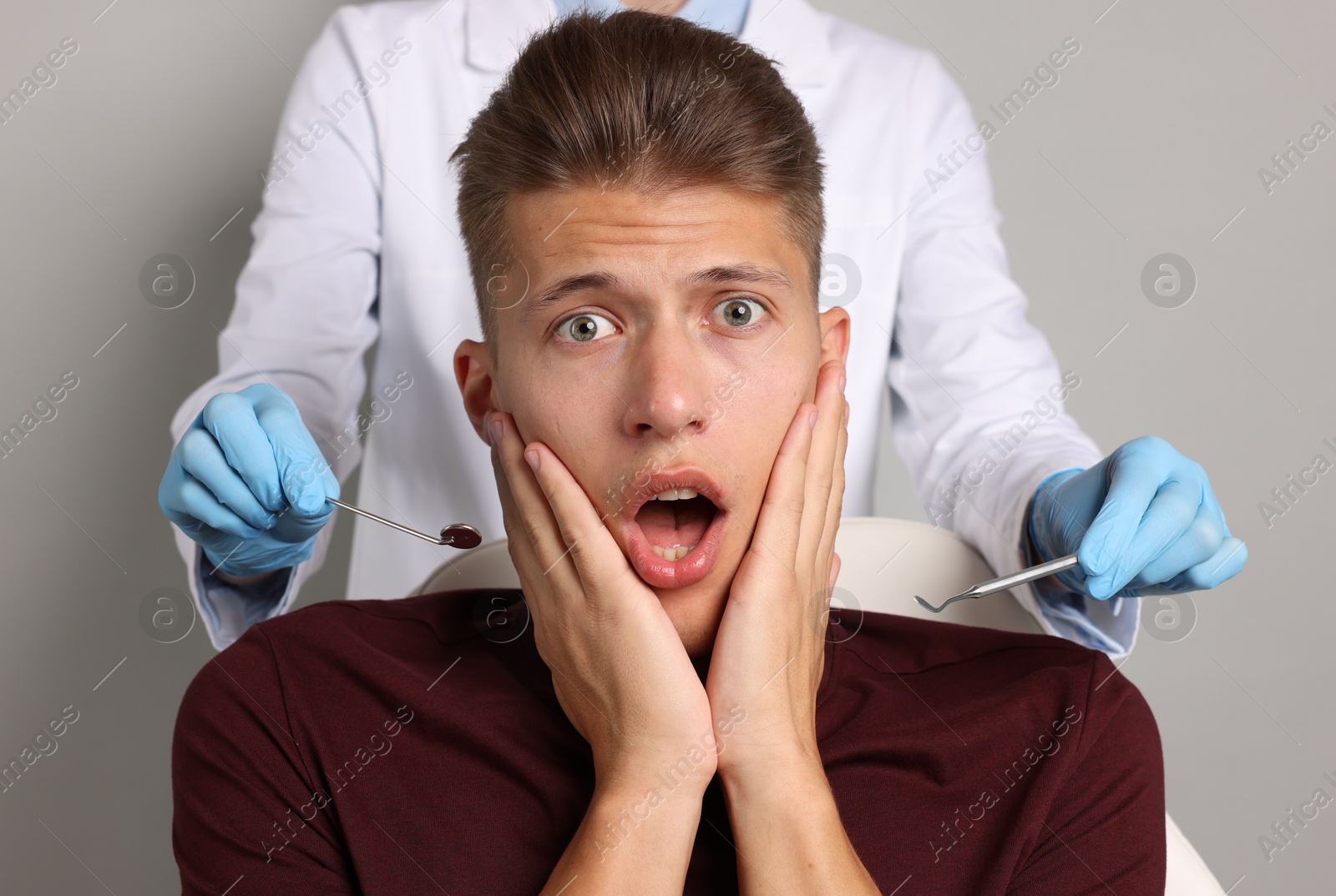 Photo of Dental phobia. Dentist working with scared man on grey background, closeup