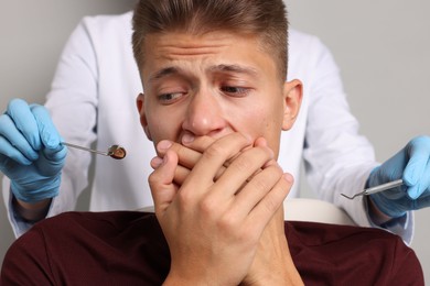 Dental phobia. Dentist working with scared man on grey background, closeup