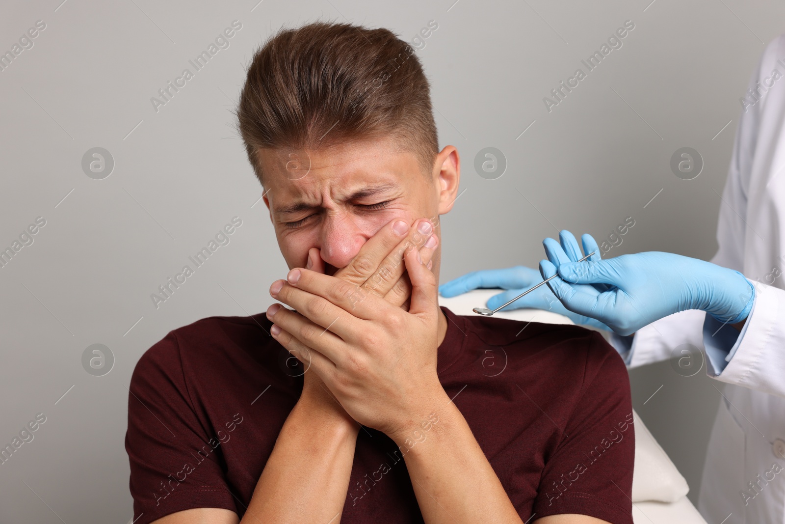 Photo of Dental phobia. Dentist working with scared man on grey background, closeup