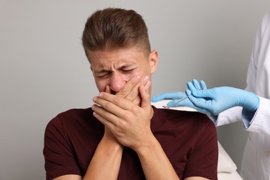 Photo of Dental phobia. Dentist working with scared man on grey background, closeup