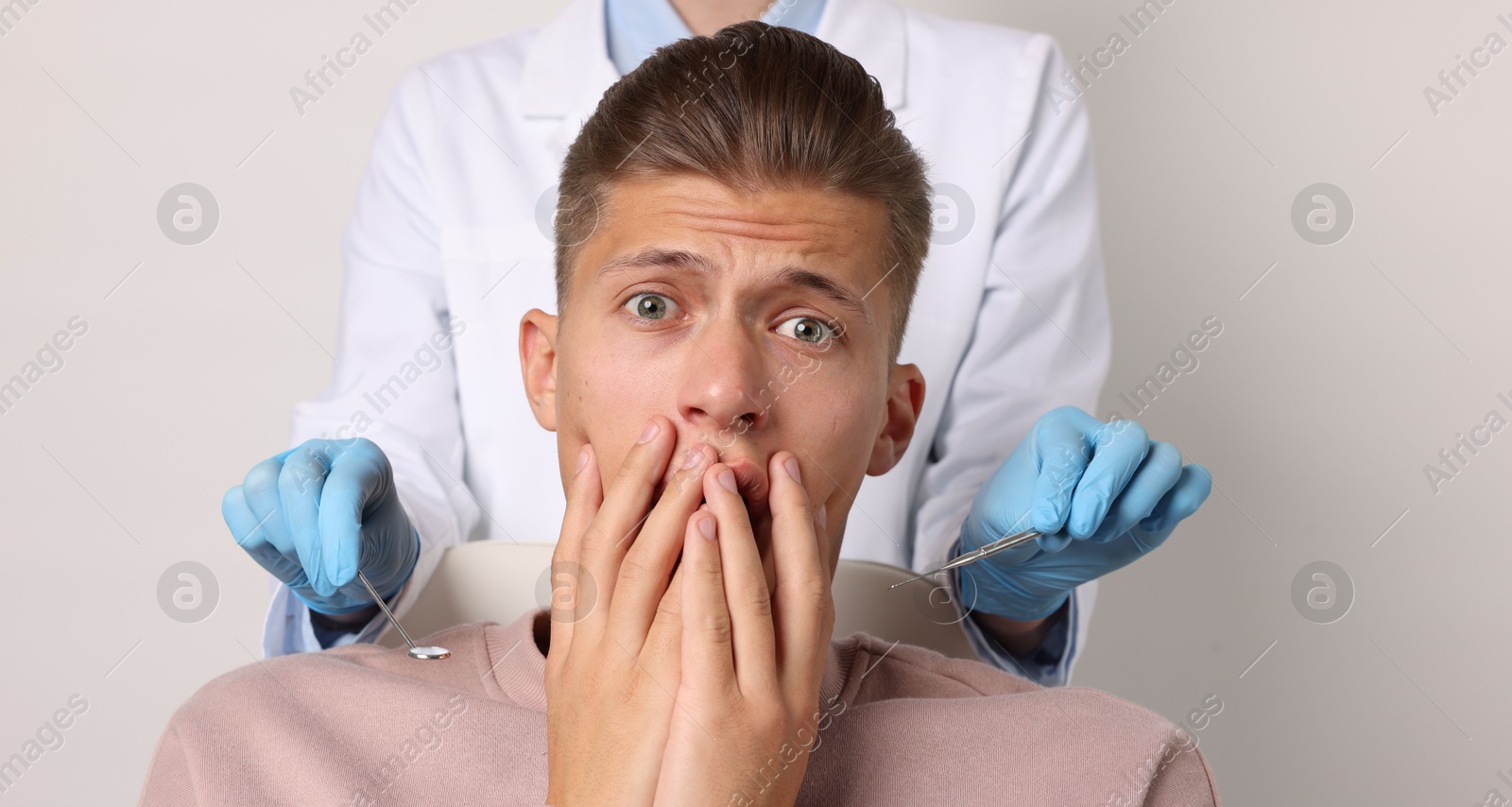 Photo of Dental phobia. Dentist working with scared man on light grey background, closeup