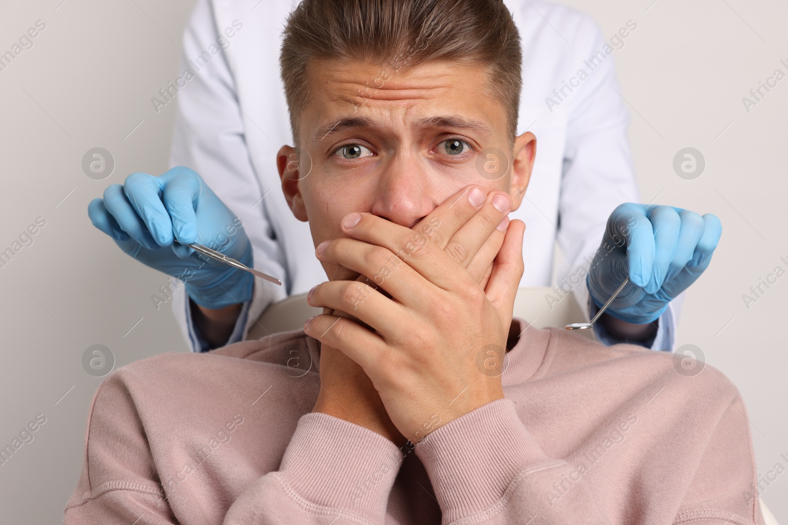 Photo of Dental phobia. Dentist working with scared man on light grey background, closeup