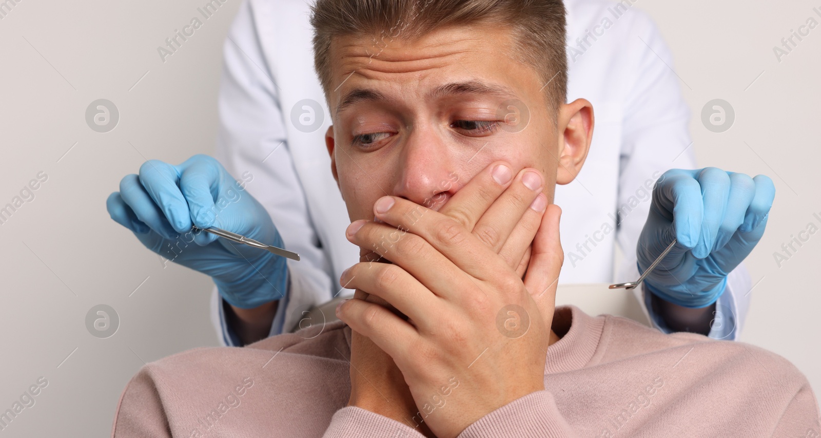 Photo of Dental phobia. Dentist working with scared man on light grey background, closeup