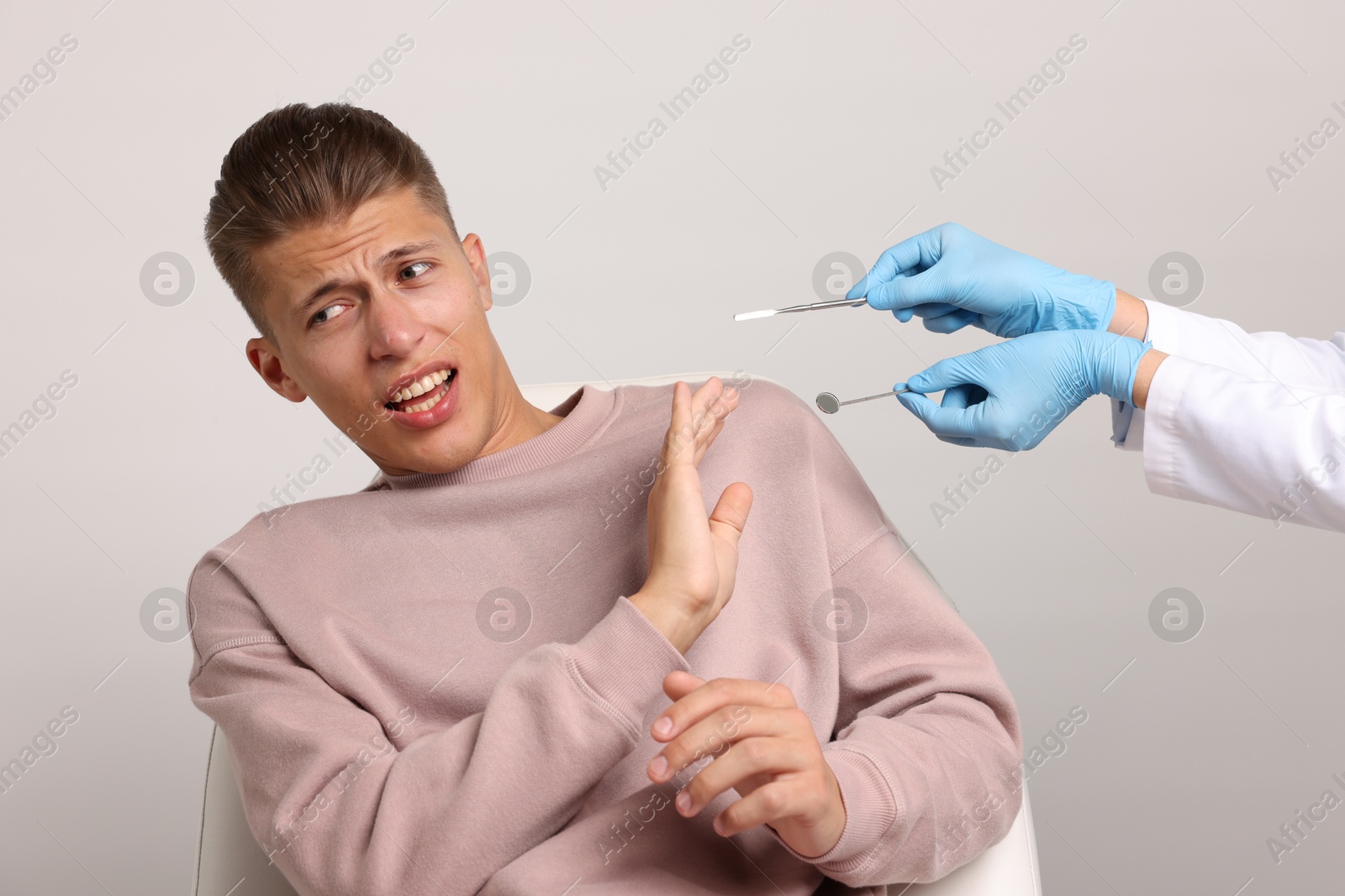 Photo of Dental phobia. Dentist working with scared man on light grey background, closeup