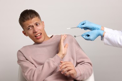 Photo of Dental phobia. Dentist working with scared man on light grey background, closeup