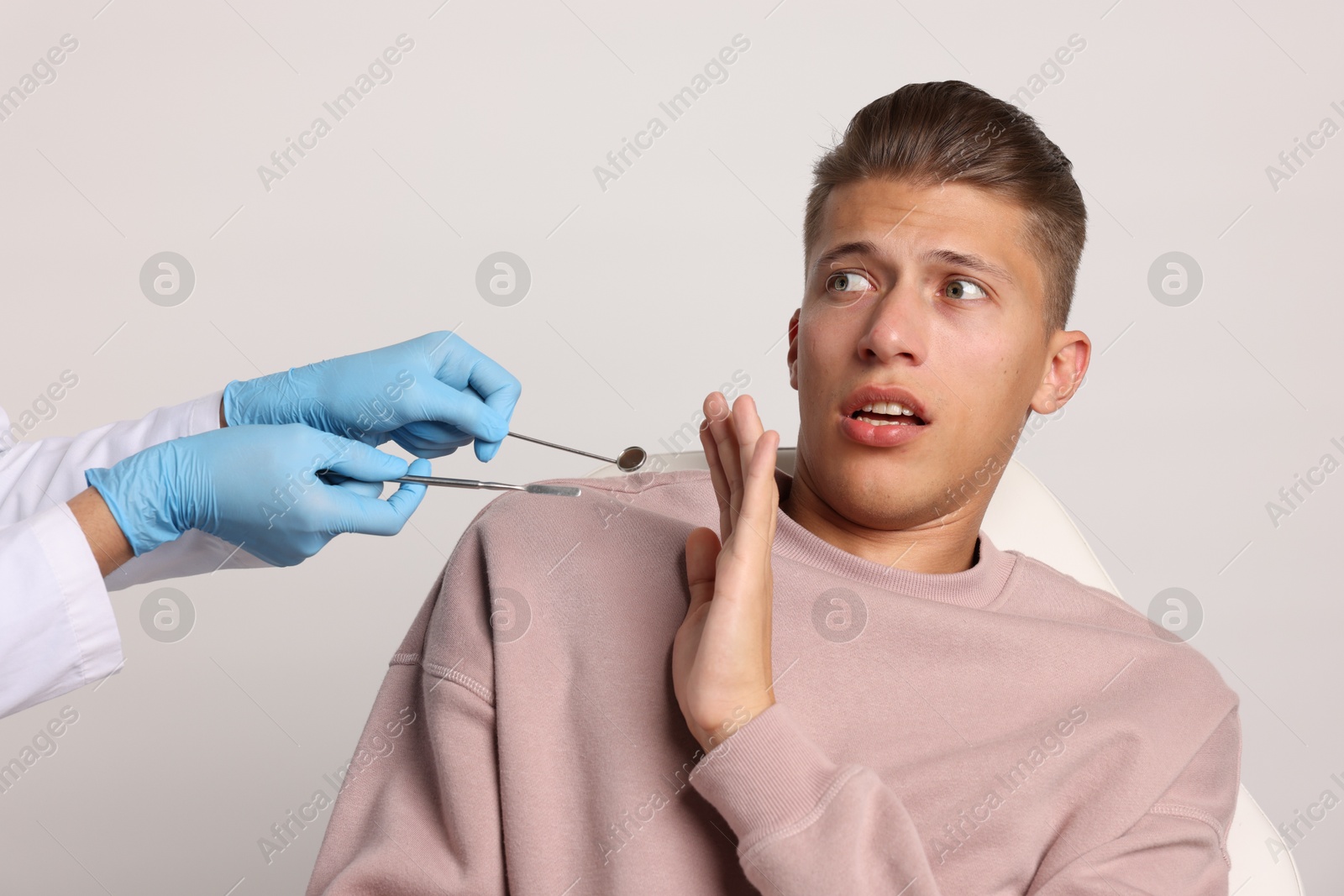 Photo of Dental phobia. Dentist working with scared man on light grey background, closeup