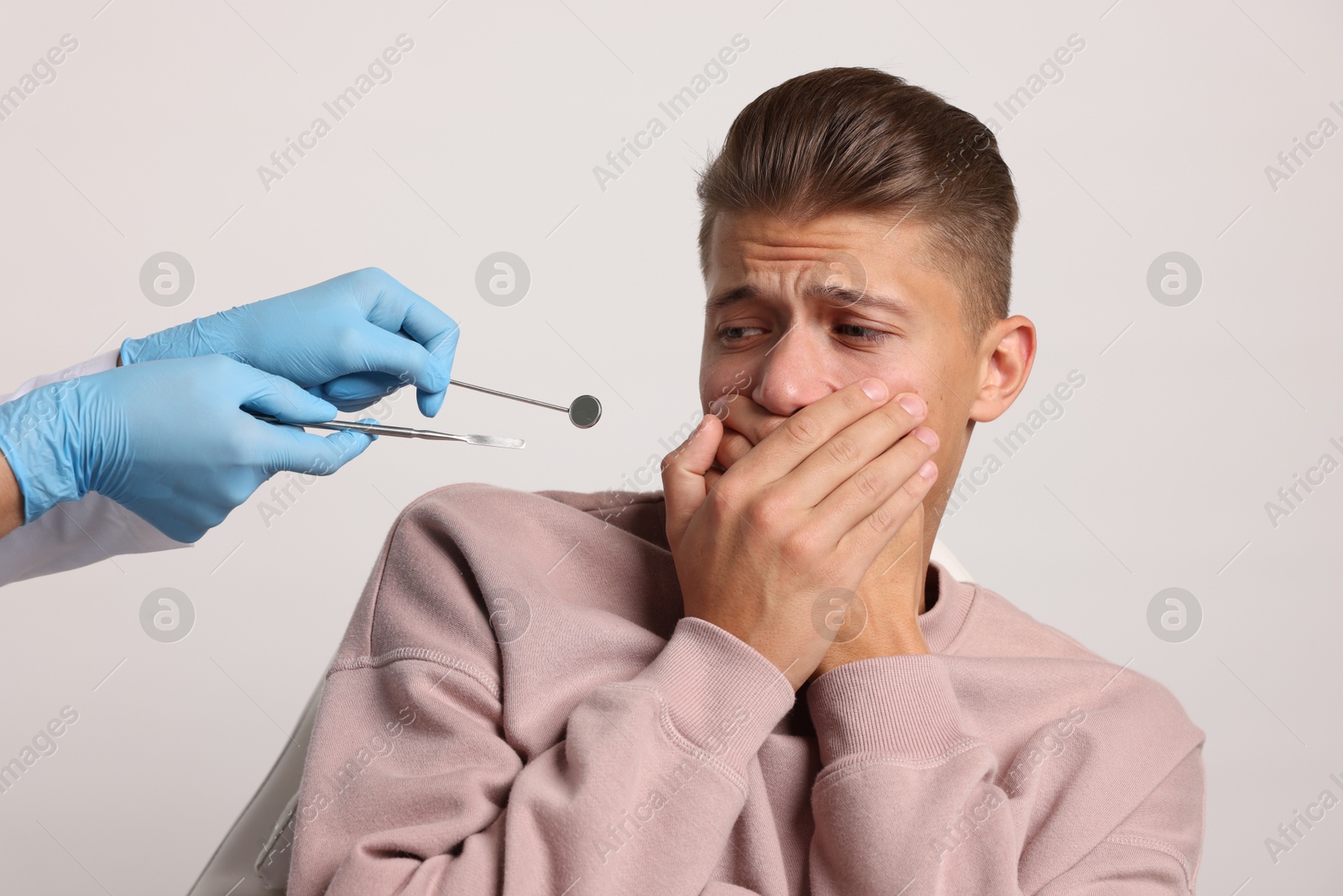 Photo of Dental phobia. Dentist working with scared man on light grey background, closeup