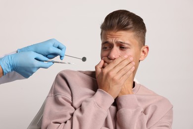 Dental phobia. Dentist working with scared man on light grey background, closeup