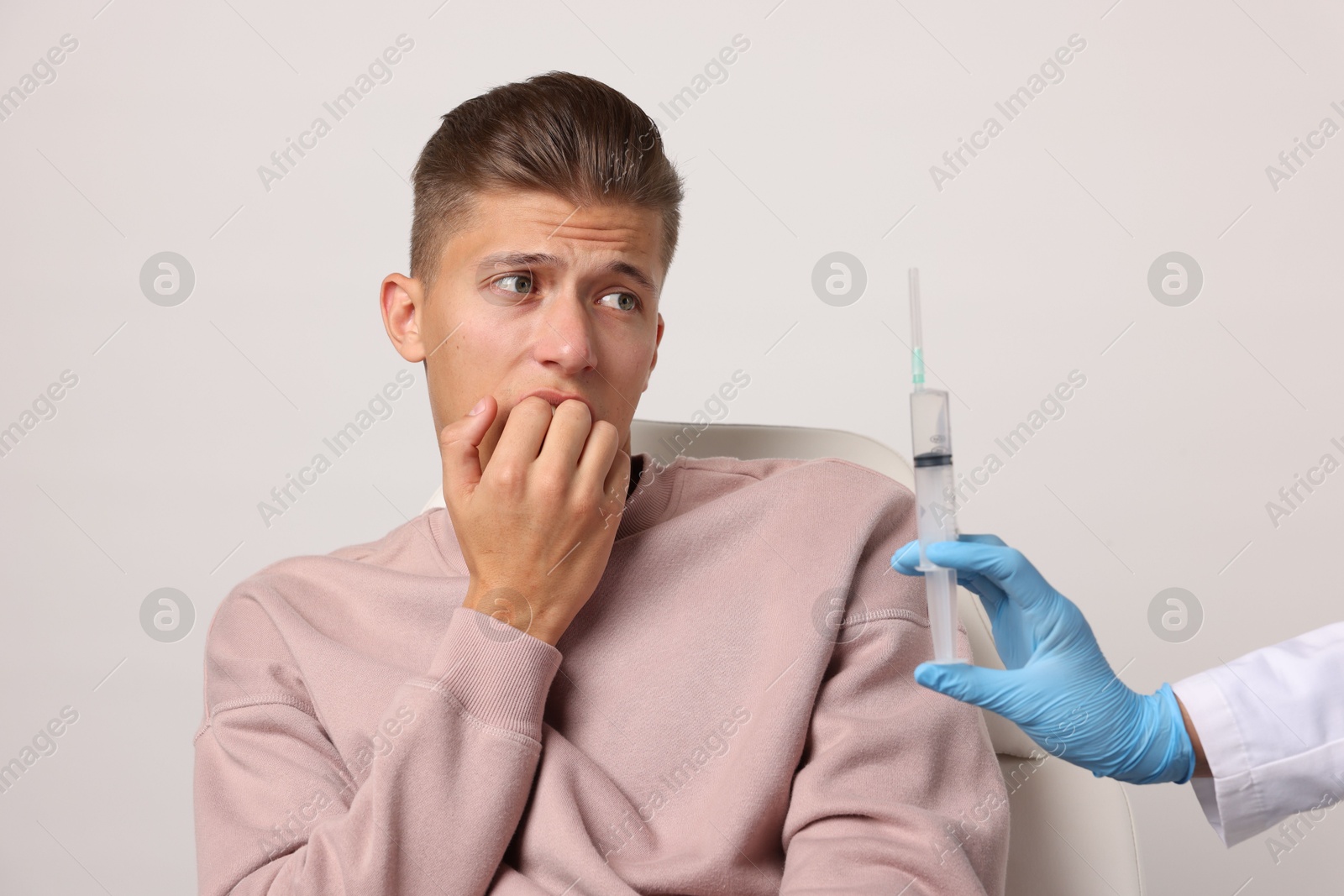 Photo of Needle phobia. Doctor with syringe near scared man on light grey background, closeup