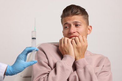 Needle phobia. Doctor with syringe near scared man on light grey background, closeup