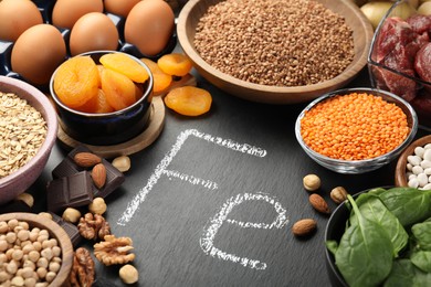 Photo of Diet plan for anemia. Different products rich in iron and slate board with Ferrum symbol on table, closeup. Space for text