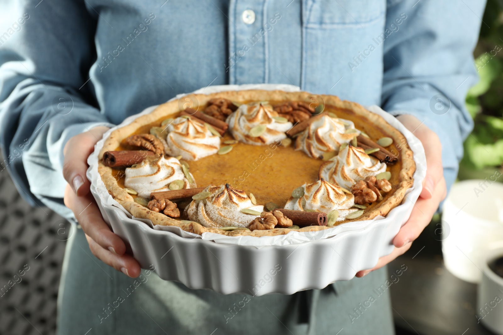 Photo of Woman holding homemade pumpkin pie with whipped cream, seeds and cinnamon on blurred background, closeup