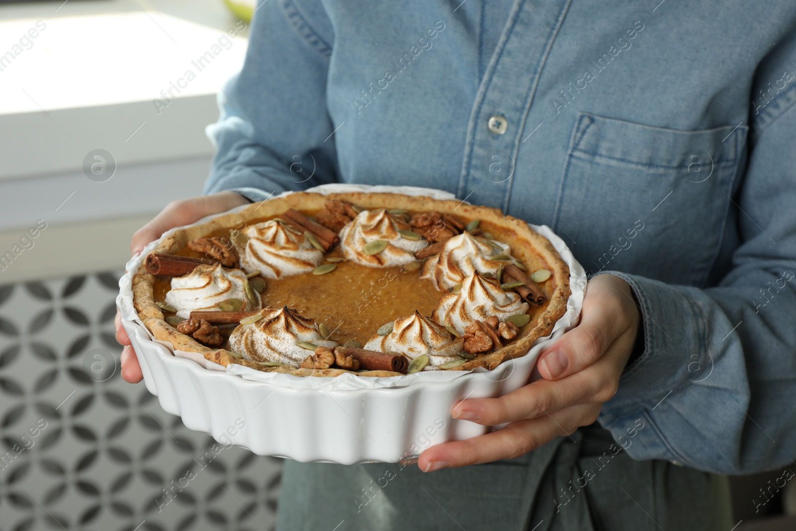 Photo of Woman holding homemade pumpkin pie with whipped cream, seeds and cinnamon on blurred background, closeup