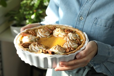 Photo of Woman holding homemade pumpkin pie with whipped cream, seeds and cinnamon on blurred background, closeup