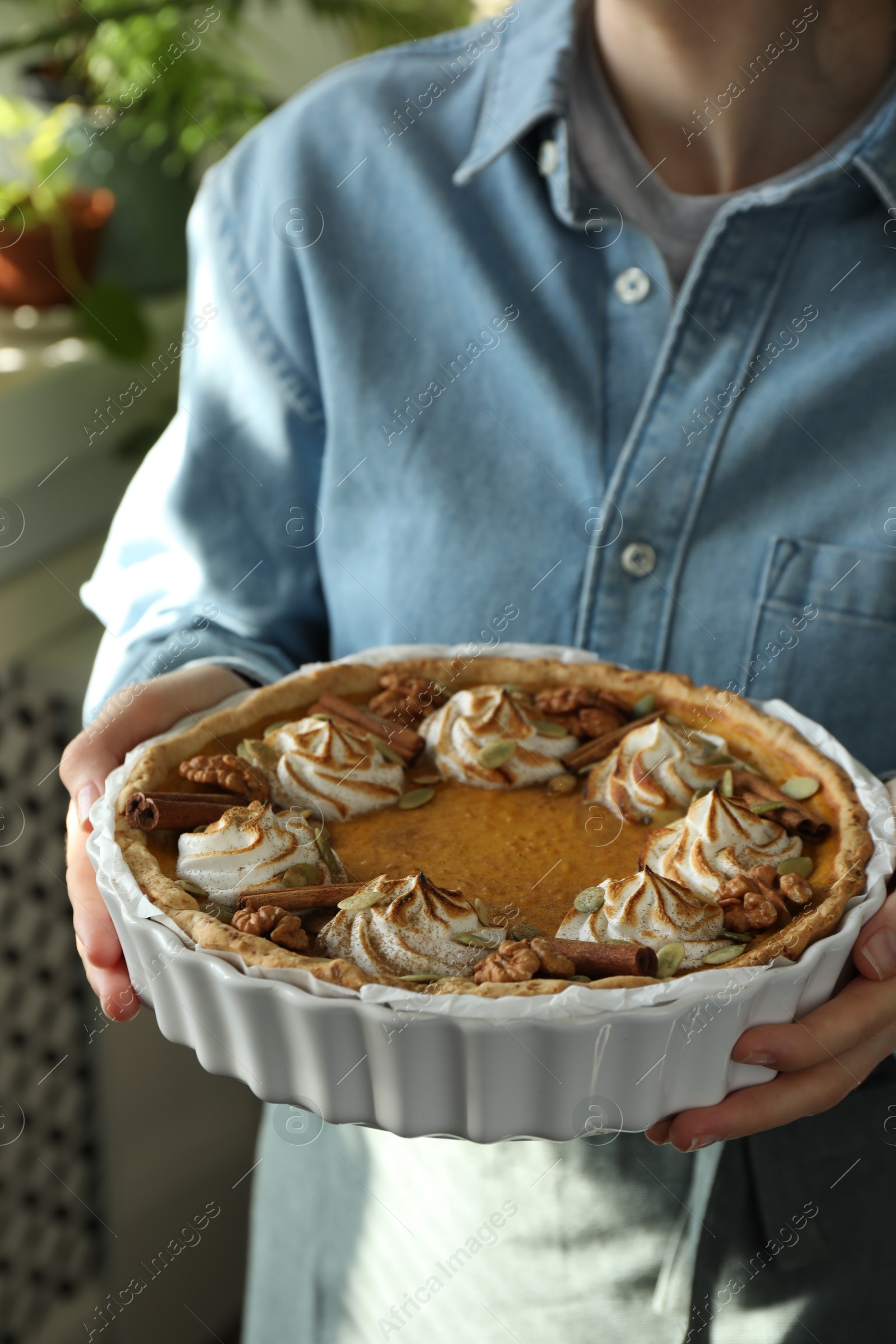 Photo of Woman holding homemade pumpkin pie with whipped cream, seeds and cinnamon on blurred background, closeup