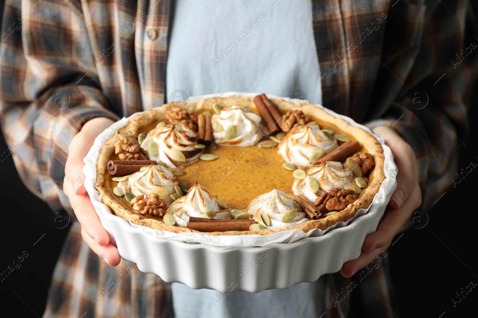 Photo of Woman holding homemade pumpkin pie with whipped cream, seeds and cinnamon on black background, closeup