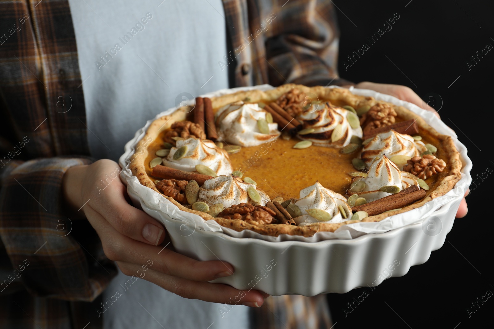 Photo of Woman holding homemade pumpkin pie with whipped cream, seeds and cinnamon on black background, closeup