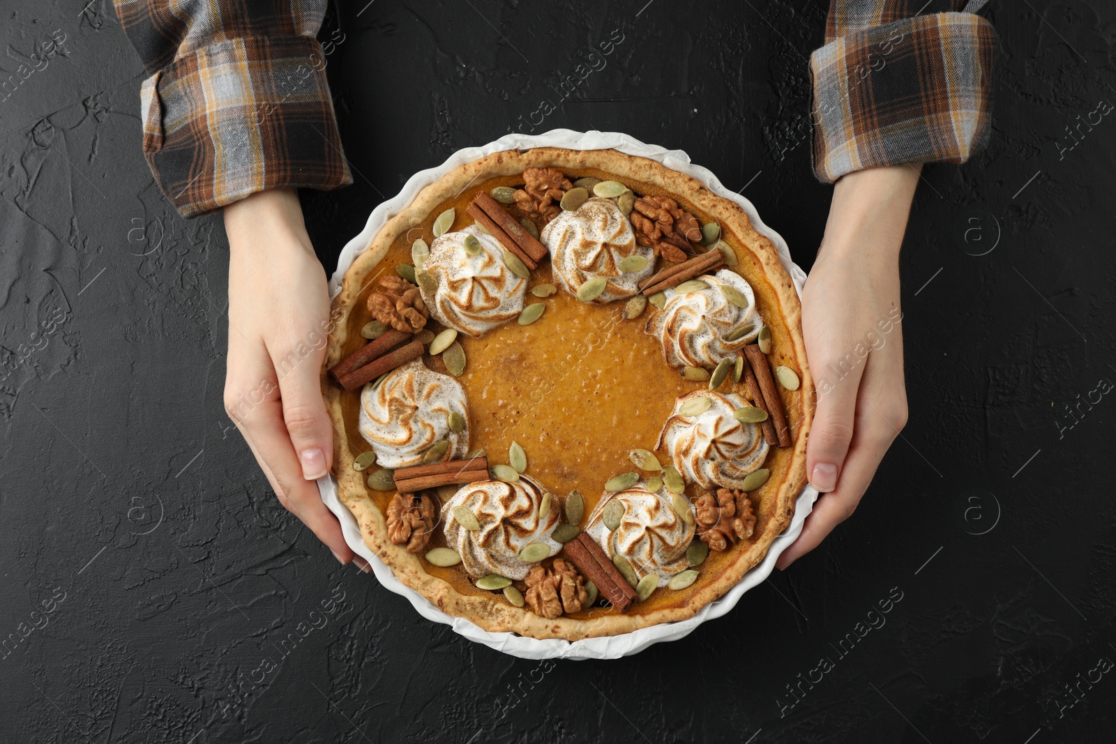 Photo of Woman with homemade pumpkin pie with whipped cream, seeds and cinnamon at black table, top view