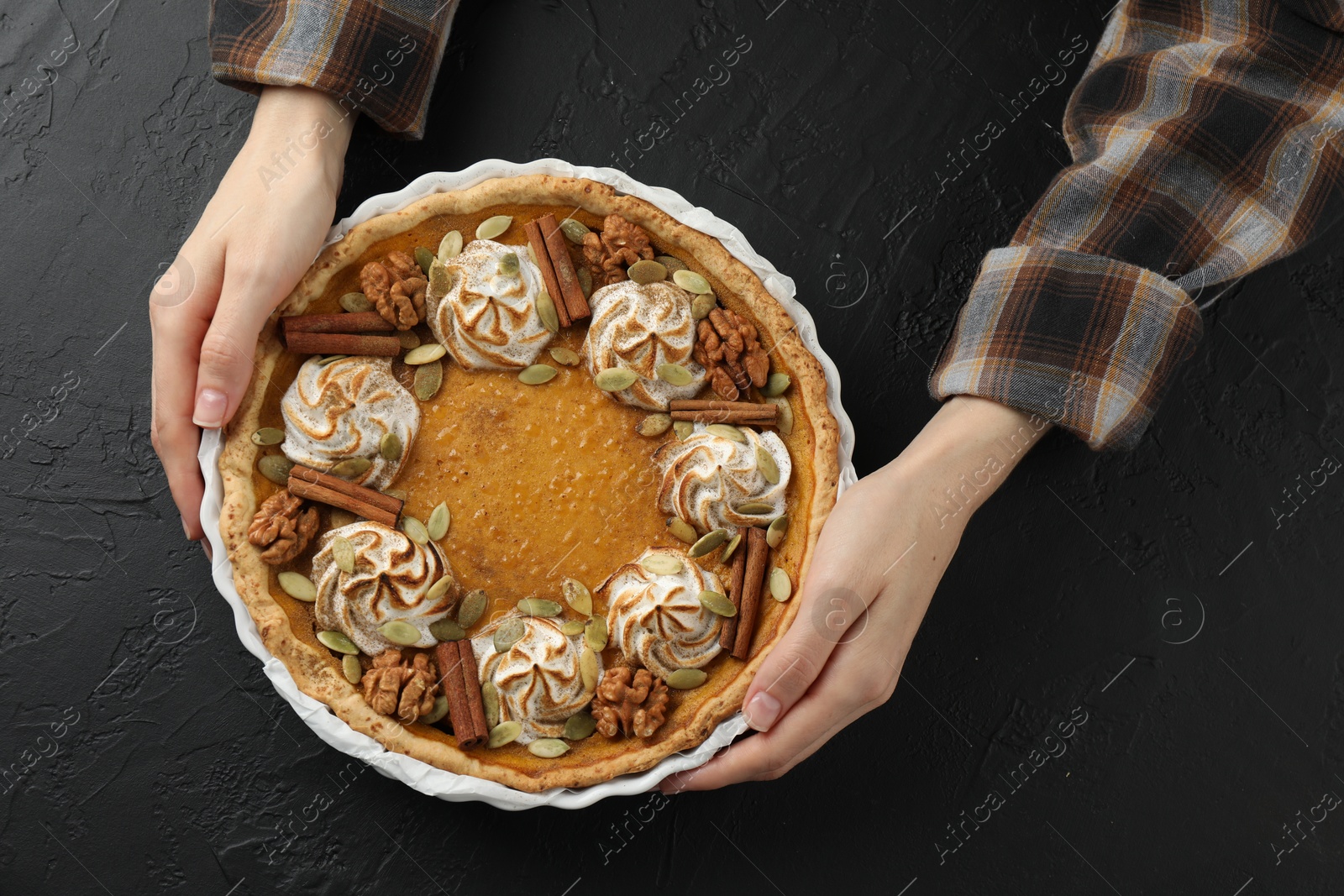 Photo of Woman with homemade pumpkin pie with whipped cream, seeds and cinnamon at black table, top view