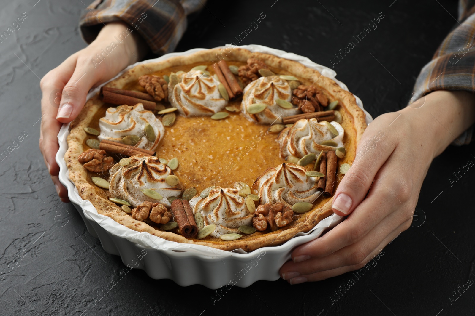 Photo of Woman with homemade pumpkin pie with whipped cream, seeds and cinnamon at black table, closeup